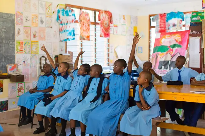 Students in blue uniforms raising their hands in a colourful classroom